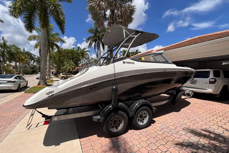 Slide: The Image of 2022 Yamaha AR210 boat on trailer, parked in sunny driveway with palm trees. - 8