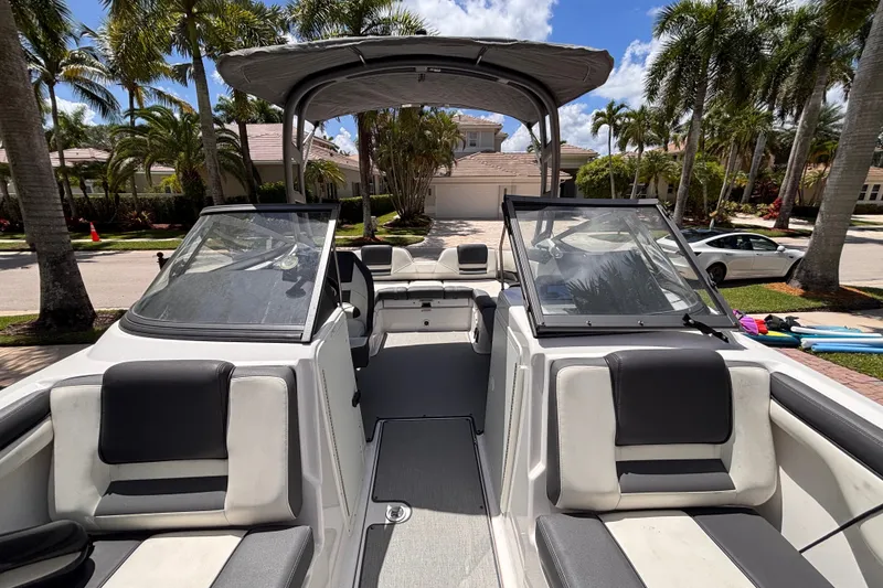 Slide: The Image of 2022 Yamaha Boats AR210 interior with seating, windshield, and canopy in a sunny driveway setting. - 37