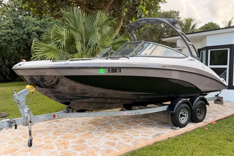 Slide: The Image of 2022 Yamaha AR210 boat on trailer, parked outdoors near lush greenery. - 2