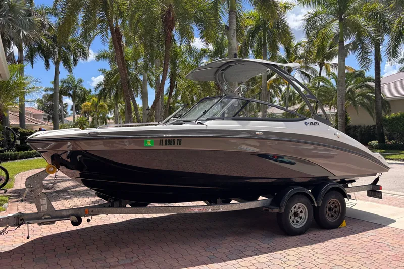 Slide: The Image of 2022 Yamaha AR210 boat on trailer, parked under palm trees in a sunny setting. - 2