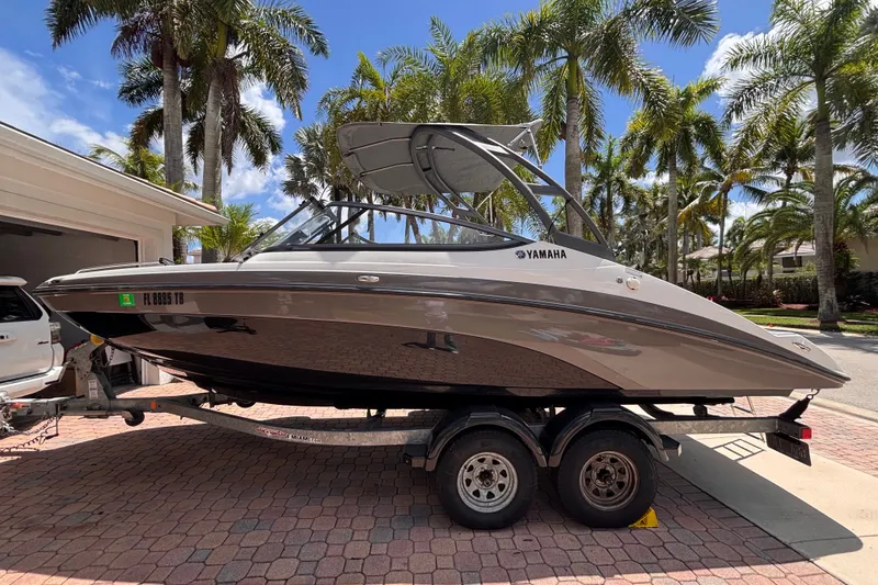 Slide: The Image of 2022 Yamaha AR210 boat on trailer, parked in a tropical driveway with palm trees. - 1