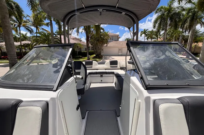Slide: The Image of 2022 Yamaha Boats AR210 interior with seating, windshield, and canopy under palm trees. - 38