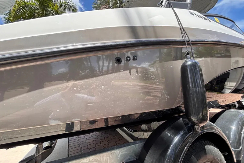 Slide: The Image of 2022 Yamaha Boats AR210 on trailer, side view with fender, palm trees in background. - 43