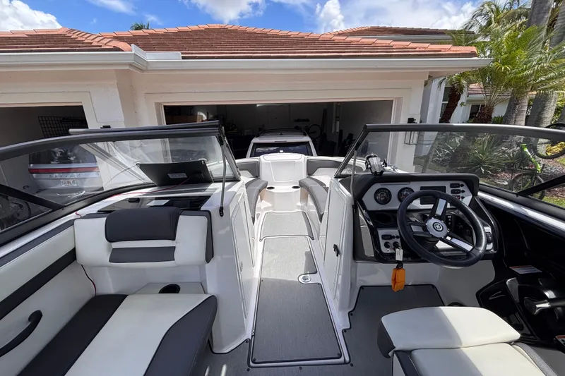 Slide: The Image of 2022 Yamaha Boats AR210 interior with steering wheel and seating, parked in a driveway. - 27