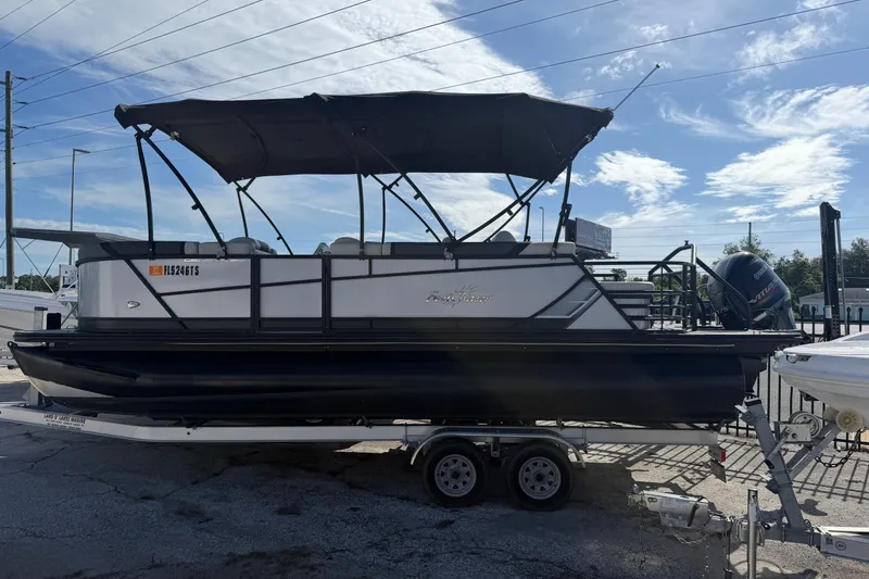 The Image of 2023 SunChaser Geneva Sport 23 SB pontoon boat on trailer under blue sky. - 0