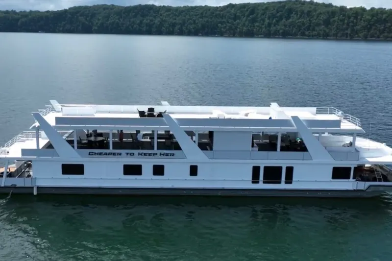 Slide: The Image of 1999 Stardust Cruisers 20 x 123 houseboat on a serene lake with lush forest backdrop. - 3