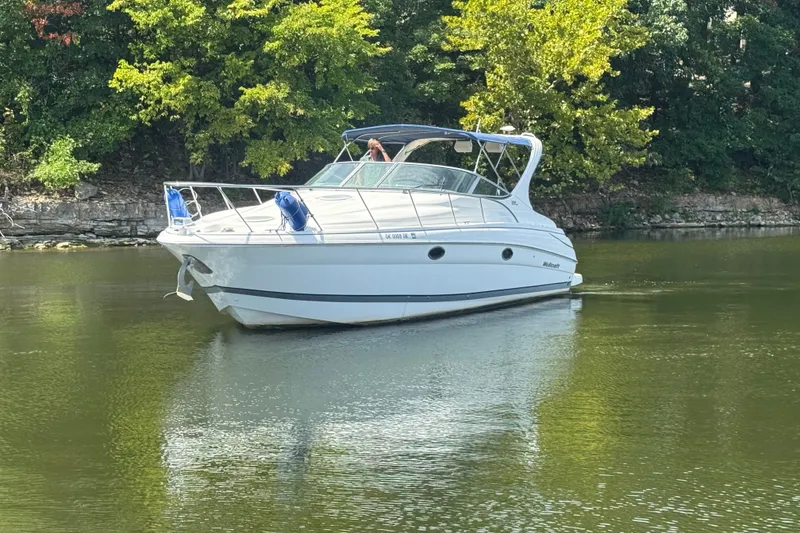 The Image of 2000 Wellcraft 3300 Martinique boat on calm water, surrounded by lush greenery. - 0