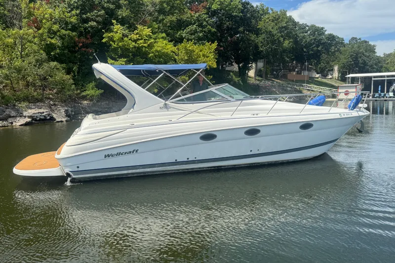 Slide: The Image of 2000 Wellcraft 3300 Martinique boat on calm water, surrounded by lush greenery. - 4