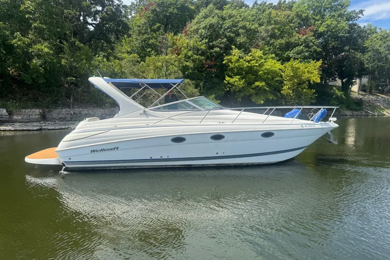 Slide: The Image of 2000 Wellcraft 3300 Martinique boat on calm water, surrounded by lush greenery. - 1