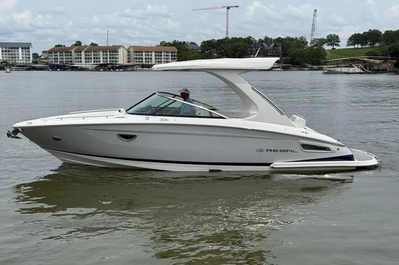Slide: The Image of 2021 Regal 2800 Bowrider boat cruising on a calm lake with scenic background. - 2