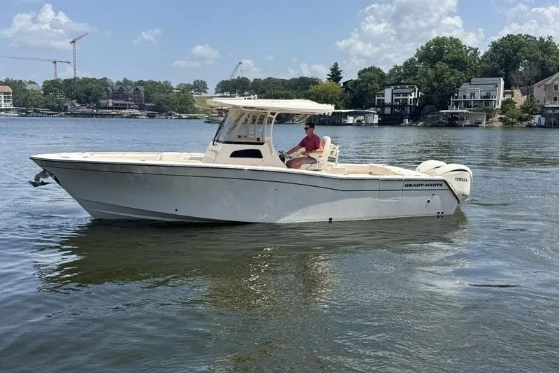 The Image of 2024 Grady-White Canyon 306 boat cruising on a scenic lake with waterfront homes. - 1