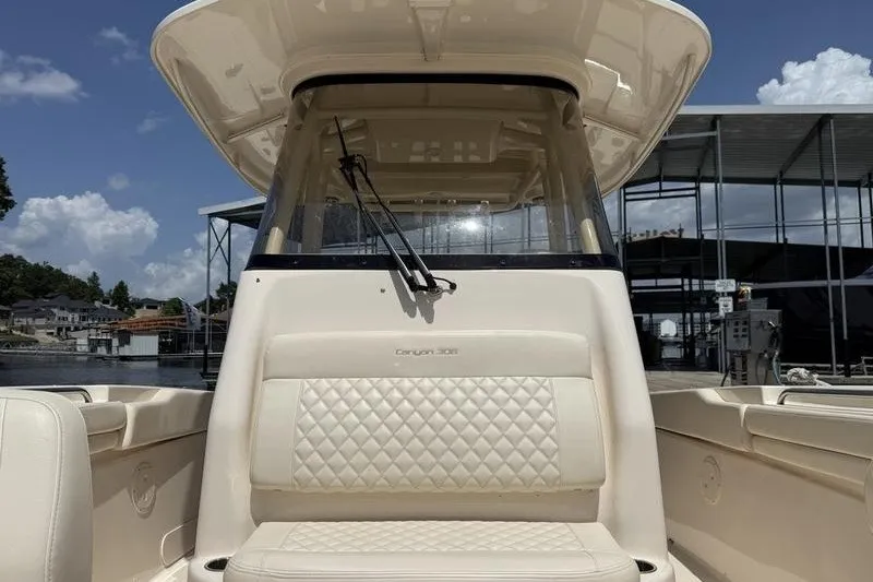 Slide: The Image of 2024 Grady-White Canyon 306 boat with cushioned seating and windshield, docked under a clear sky. - 14