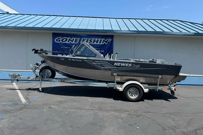 The Image of 2021 Hewescraft 180 River Runner boat on trailer, parked outside a building. - 0