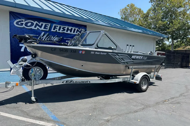 Slide: The Image of 2021 Hewescraft 180 River Runner boat on EZ Loader trailer outside marine dealership. - 1