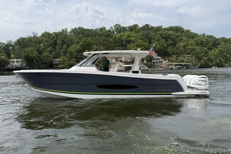 Slide: The Image of 2021 Regal 38 SAV boat cruising on a lake with lush green shoreline. - 5