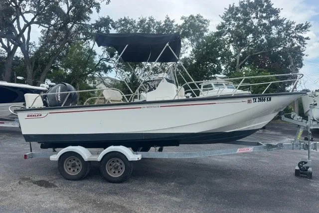 Slide: The Image of 2022 Boston Whaler 190 Montauk boat on trailer, parked outdoors with trees in background. - 1