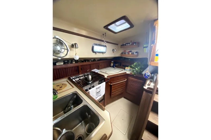 Slide: The Image of Cozy 1989 Island Packet 35 yacht kitchen with stove, sink, and storage shelves. - 12