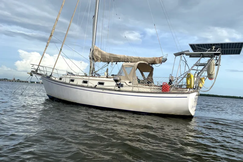 Slide: The Image of 1989 Island Packet 35 sailboat on calm water, featuring solar panels and beige sails. - 2