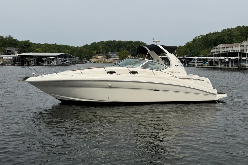 The Image of 2003 Sea Ray Sundancer 320 yacht on calm water, surrounded by docks and greenery. - 0