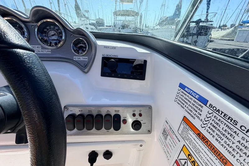Slide: The Image of 2026 NauticStar 203 DC Deck boat dashboard with gauges and safety notices. - 13