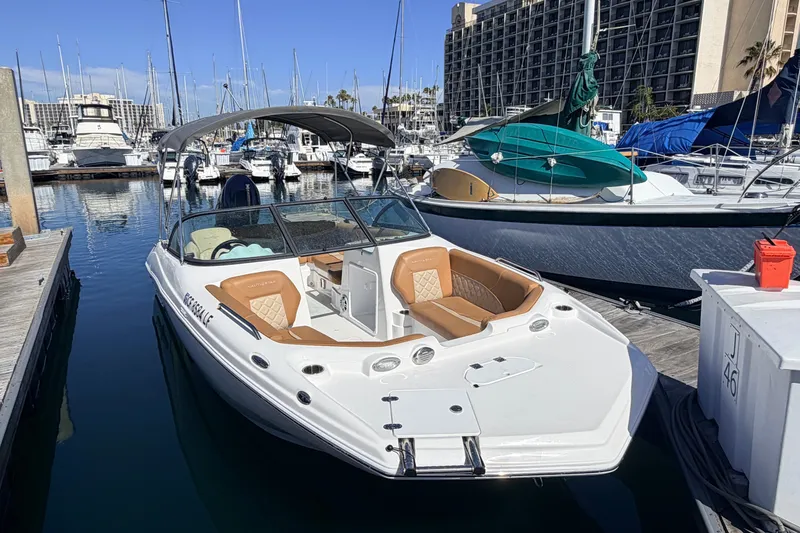 The Image of 2026 NauticStar 203 DC Deck boat docked in a marina, featuring tan seating and a bimini top. - 1