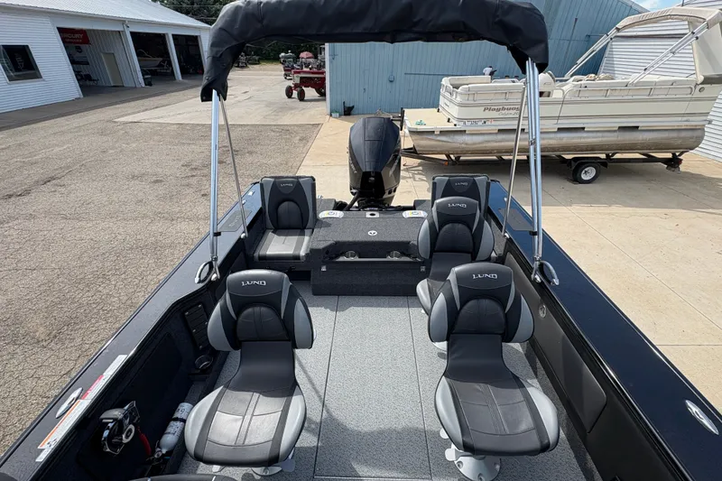 Slide: The Image of 2025 Lund 1875 Pro-V boat interior with four seats and a motor, docked outdoors. - 31