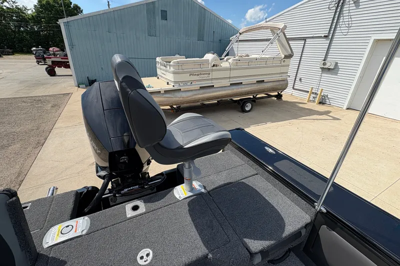 Slide: The Image of 2025 Lund 1875 Pro-V boat interior with seating and motor, parked near a pontoon. - 44