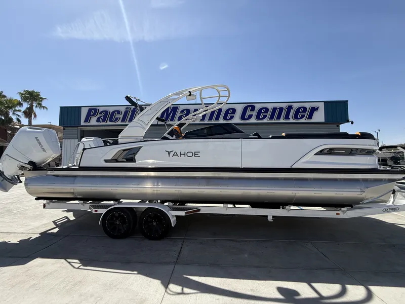 The Image of A luxurious Tahoe pontoon boat with twin Mercury V10 engines, on a trailer in front of a marine center. - 1