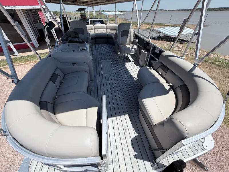 Slide: The Image of A spacious pontoon boat with beige cushioned seating and an open deck, docked by a lake. - 9