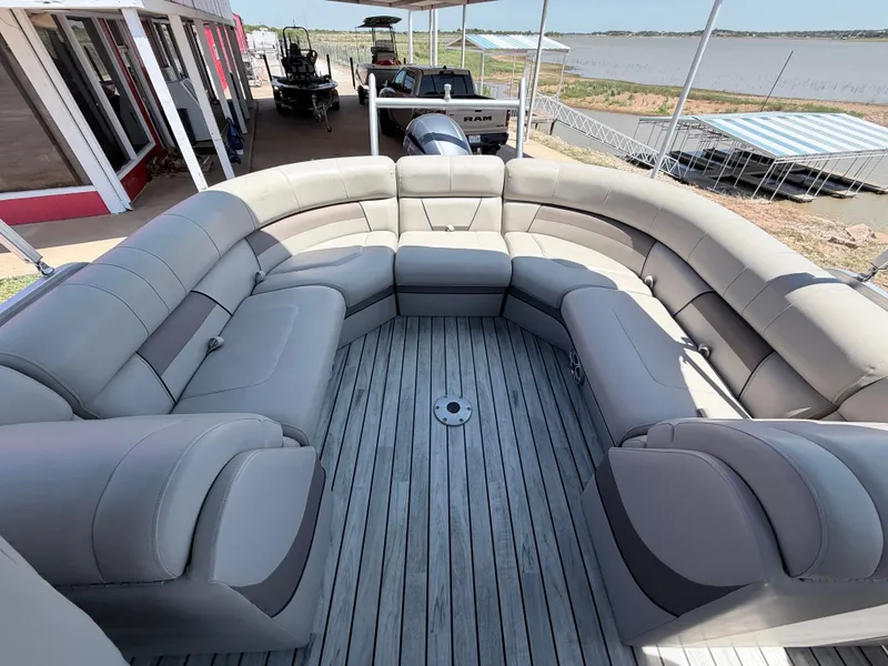 Slide: The Image of A luxurious pontoon boat with gray cushioned seating and wooden flooring, docked by a lakeside. - 11