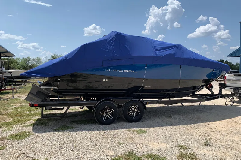 Slide: The Image of 2020 Regal LS6 Surf boat covered with blue tarp on trailer under clear sky. - 76