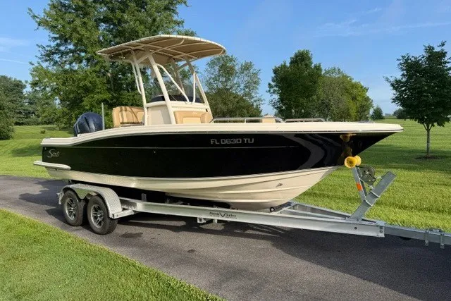 The Image of 2020 Scout 215 XSF boat on trailer, parked on a driveway with lush greenery. - 0