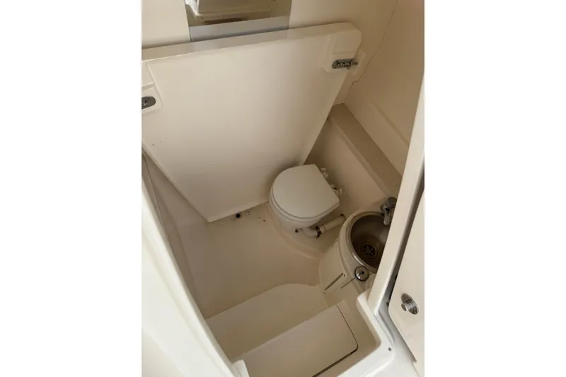 Slide: The Image of Compact bathroom in 2014 Intrepid 327 Center Console boat, featuring toilet and sink. - 15