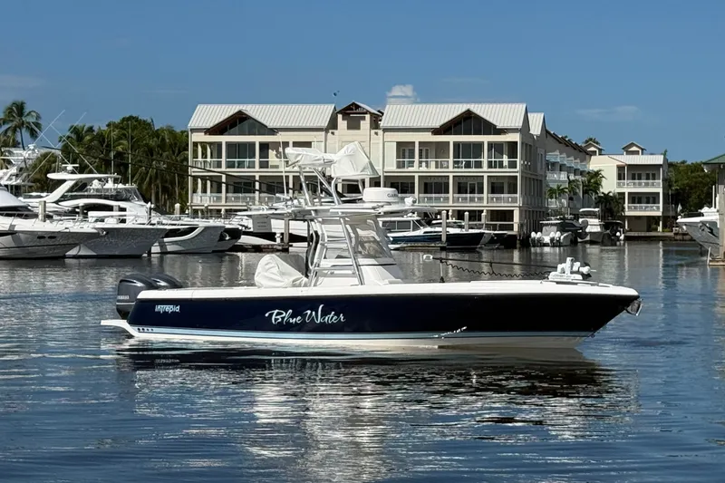 The Image of 2014 Intrepid 327 Center Console boat docked in marina, with waterfront buildings in background. - 0