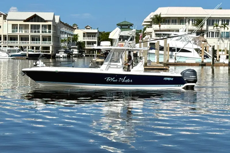 Slide: The Image of 2014 Intrepid 327 Center Console boat docked in a marina, surrounded by buildings. - 2