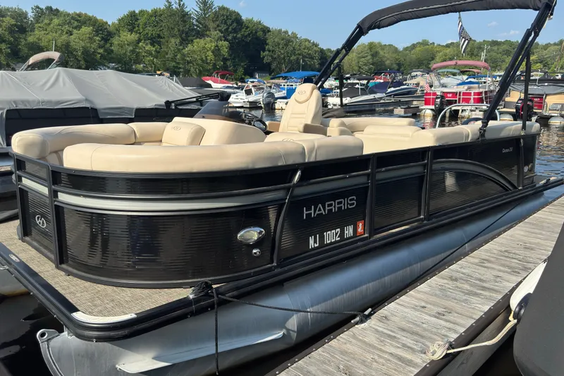 Slide: The Image of 2020 Harris Cruiser 210 pontoon boat docked, featuring beige seating and sleek black exterior. - 1
