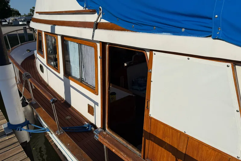 Slide: The Image of 1982 Albin 36 Trawler with blue canopy, docked, showcasing wooden deck and cabin details. - 5