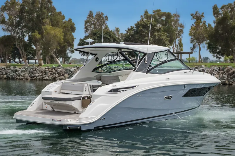 The Image of The 2025 Sea Ray 320 Sundancer DA Coupe cruises on calm water, surrounded by trees. - 0