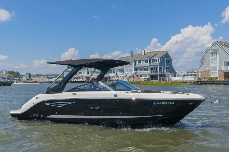The Image of A black 2016 Sea Ray SLX 250 boat cruising on a river with modern houses in the background. - 0
