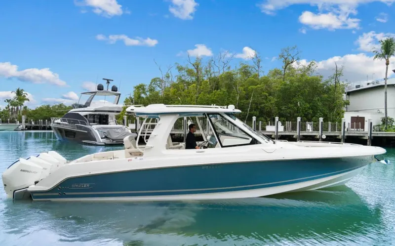 Slide: The Image of 2022 Boston Whaler 380 Realm boat on calm water, clear sky, and lush greenery background. - 2