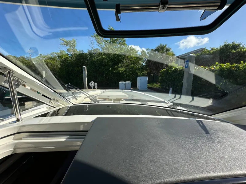 Slide: The Image of 2022 Boston Whaler 380 Realm cockpit view with open windshield, surrounded by greenery. - 28