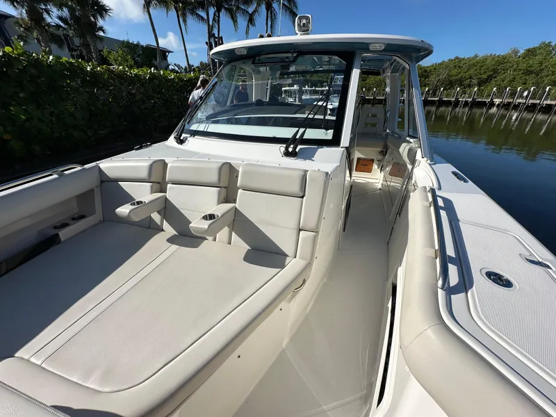 Slide: The Image of 2022 Boston Whaler 380 Realm boat interior with seating and console, docked by lush greenery. - 24