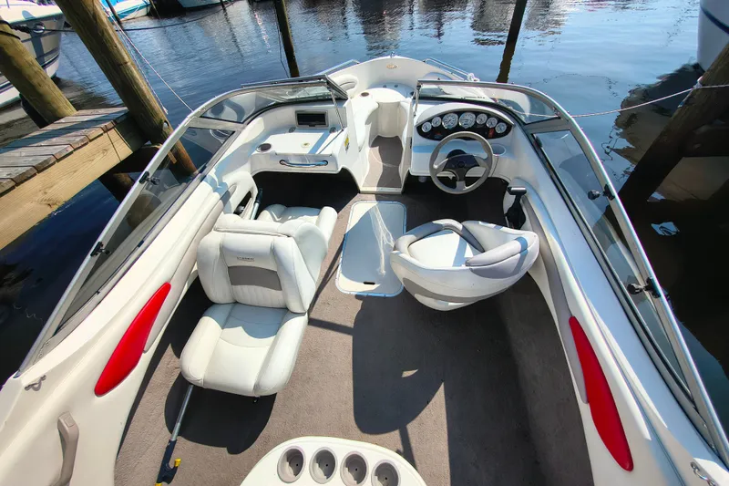 Slide: The Image of 2004 Stingray 185 LS/LX boat interior with white seating and dashboard, docked by the water. - 2