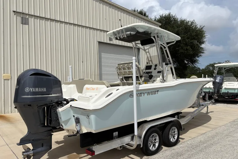 Slide: The Image of 2025 Key West 239 FS boat with Yamaha engine on trailer, parked outside a warehouse. - 2
