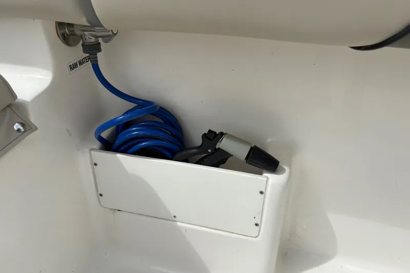 Slide: The Image of Key West 239 FS 2025 boat raw water hose storage compartment with coiled blue hose. - 28