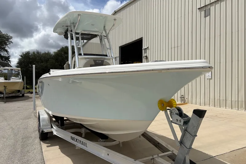 Slide: The Image of 2025 Key West 239 FS boat on trailer, parked outside a metal building under cloudy skies. - 12