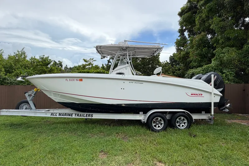 The Image of 2006 Boston Whaler 270 Outrage boat on trailer, parked on grass. - 1