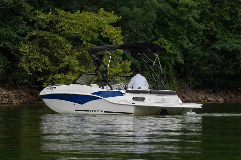 Slide: The Image of 2023 Starcraft SVX 210 IO boat cruising on a serene lake with lush greenery. - 1