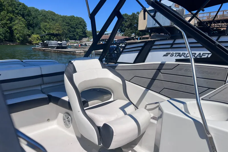 Slide: The Image of 2023 Starcraft SVX 210 IO boat interior with seating, docked by a scenic lake. - 7