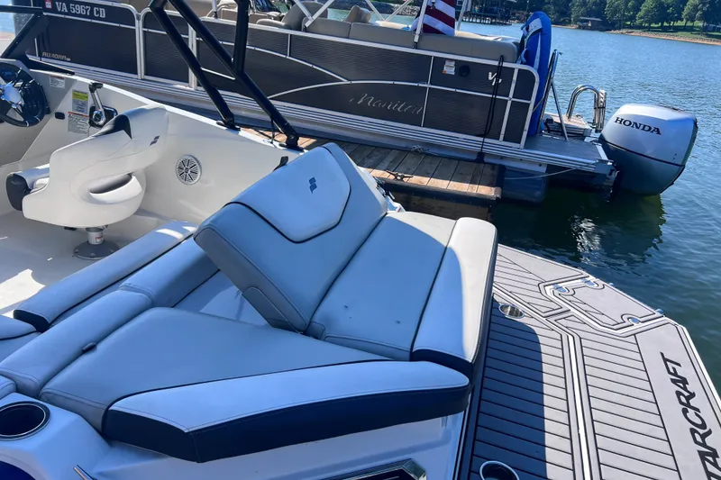 Slide: The Image of 2023 Starcraft SVX 210 IO boat interior with seating, docked near a pontoon boat. - 12